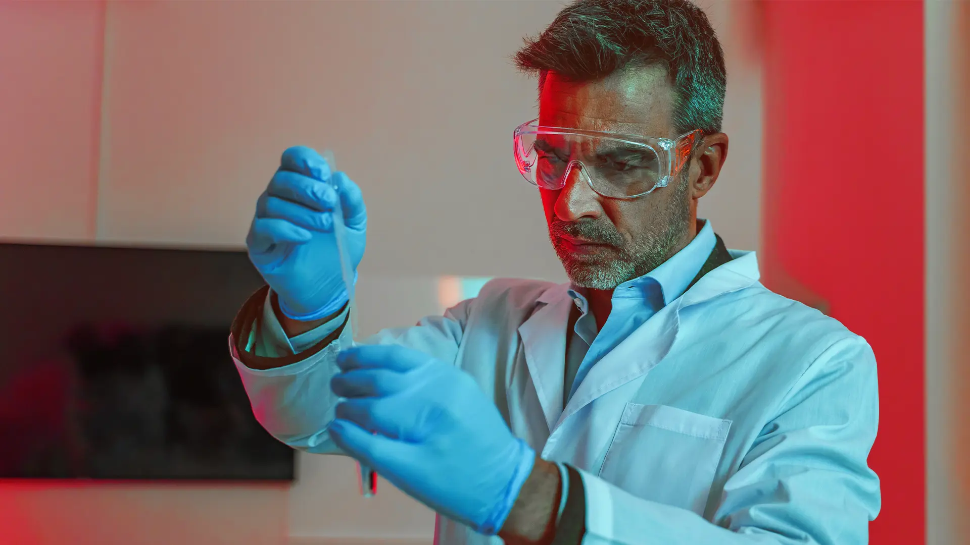 Scientist in protective eyewear and gloves examining a laboratory sample during pharmaceutical development