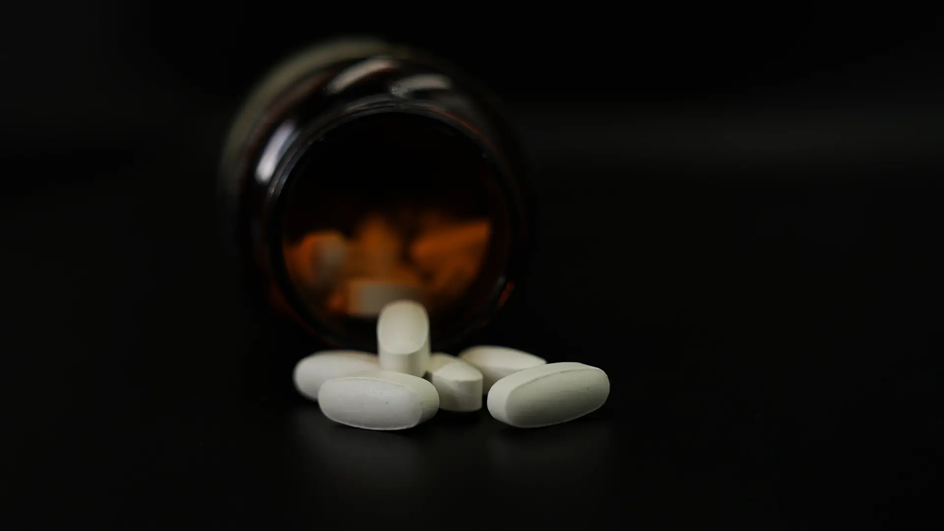 A close-up of white oral tablets emerging from a brown pharmaceutical bottle, representing PCI Pharma Services’ expertise in enabling oral delivery of targeted protein degraders (TPDs) for oncology applications.
