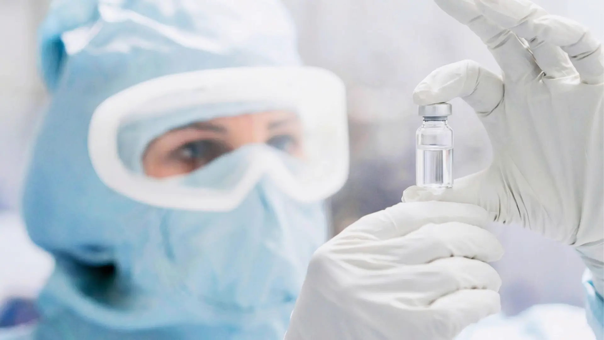 Scientist in sterile cleanroom PPE inspecting a pharmaceutical vial, representing sterile liquid drug development and integrated biologics manufacturing