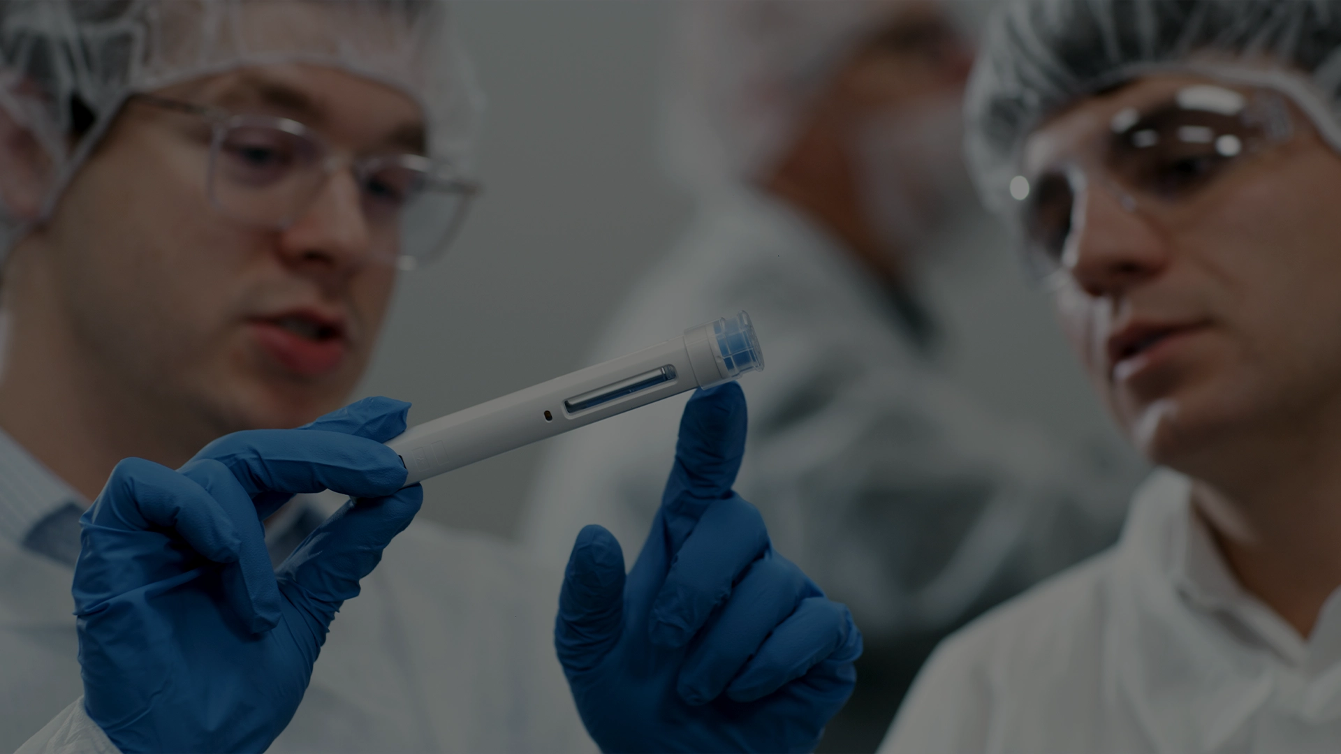 Scientists in a cleanroom examining an autoinjector device during clinical trial preparation, highlighting PCI Pharma Services’ expertise in autoinjectors in clinical trials and drug delivery solutions