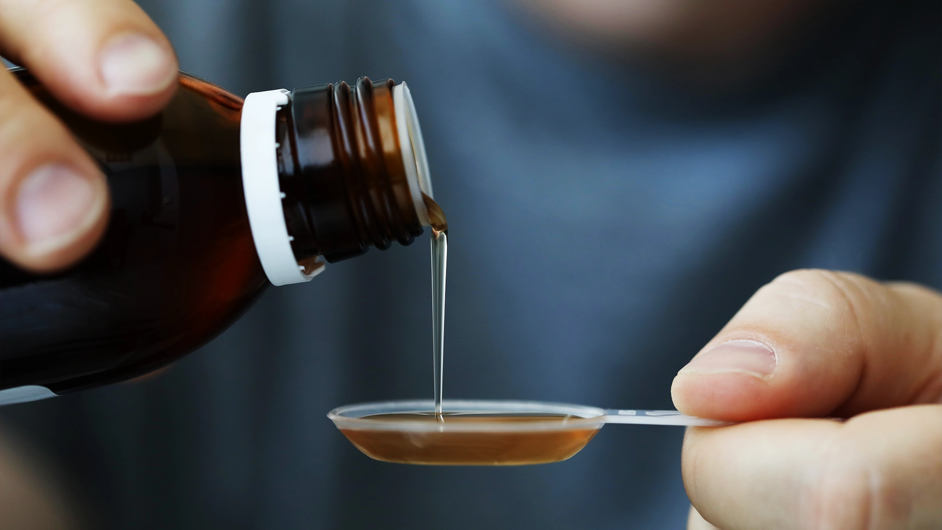 Person pouring an oral liquid medicine into a measuring spoon, representing oral liquid formulations used for precise dosing and patient-centric drug delivery.